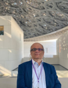 Headshot of Nasser Rabbat, who wears a blue blazer, collared shirt, purple lanyard, and glasses.