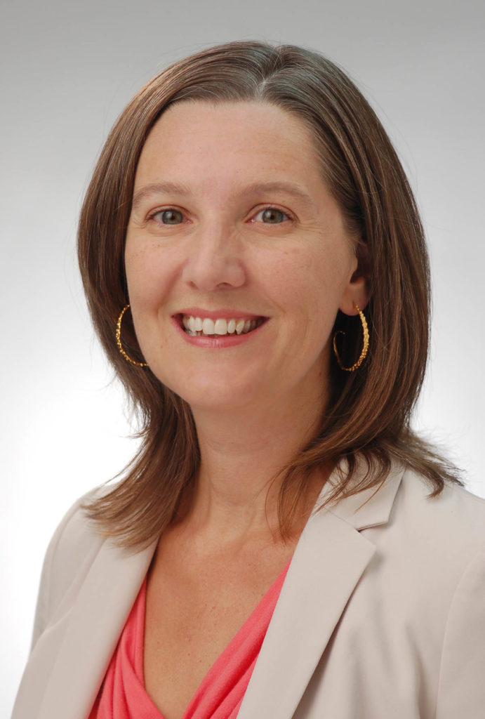 Headshot of Melissa Blair, who wears hoop earrings, a cream-colored blazer, and a pink shirt. She has shoulder length light brown hair.