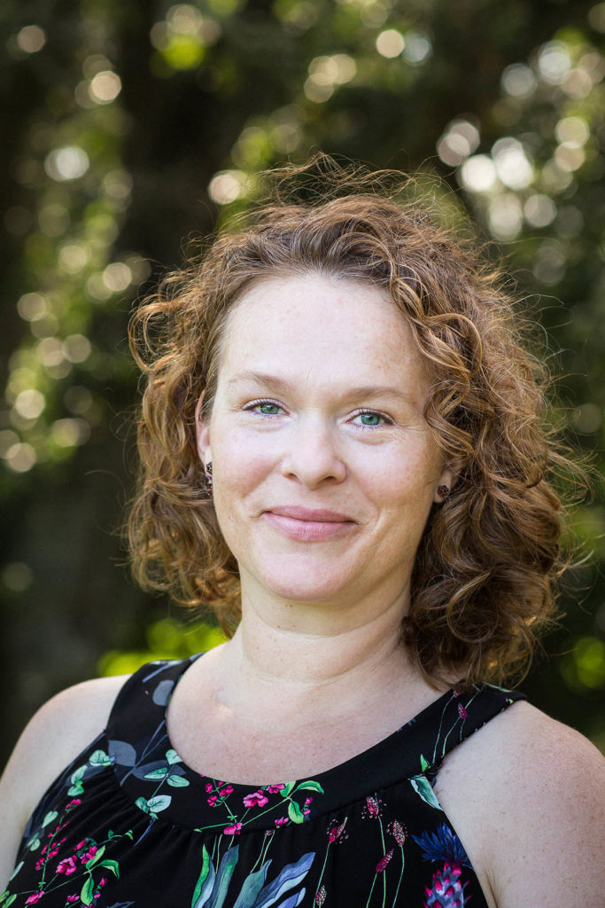 Headshot of Andrea Mosterman, who stands outdoors and wears a black shirt with colorful flowers.