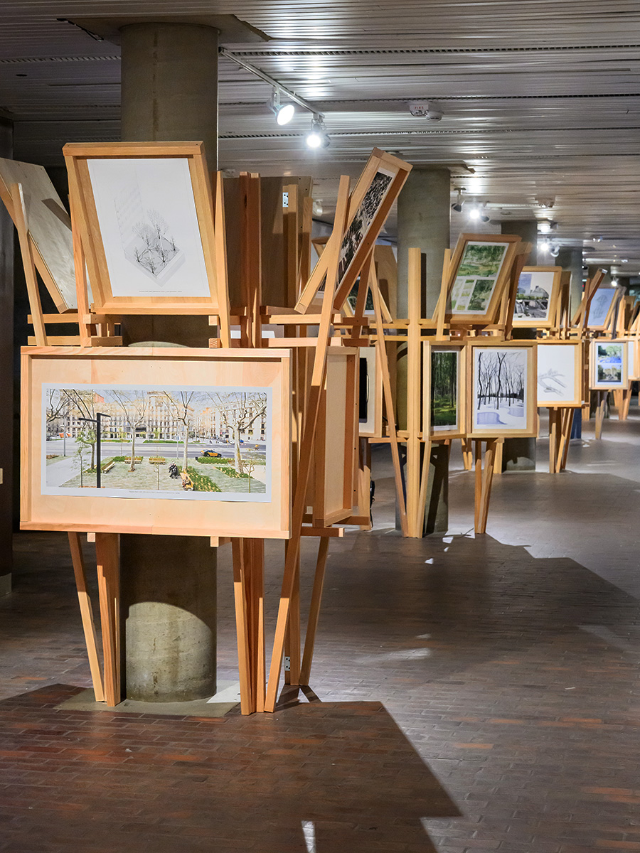 A view inside Druker Design Gallery showing a row of columns with large wooden structures built around each including images on wooden display panels.
