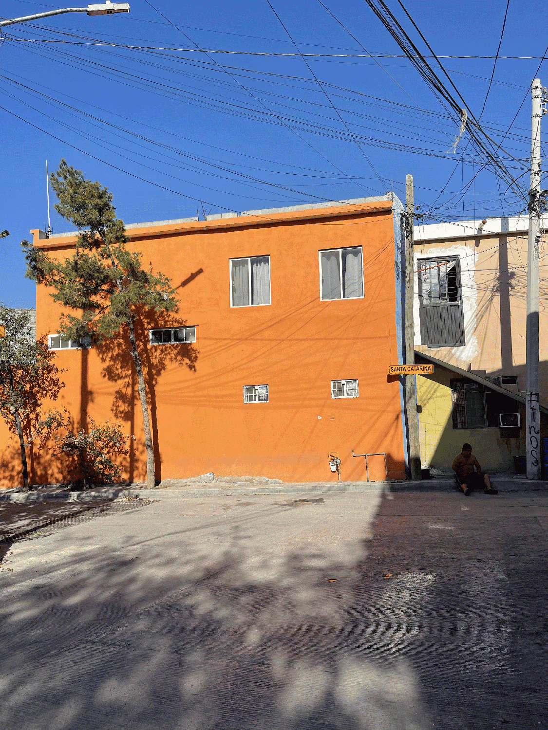 Colorful buildings under a blue sky. A man sits on a curb in the shade.