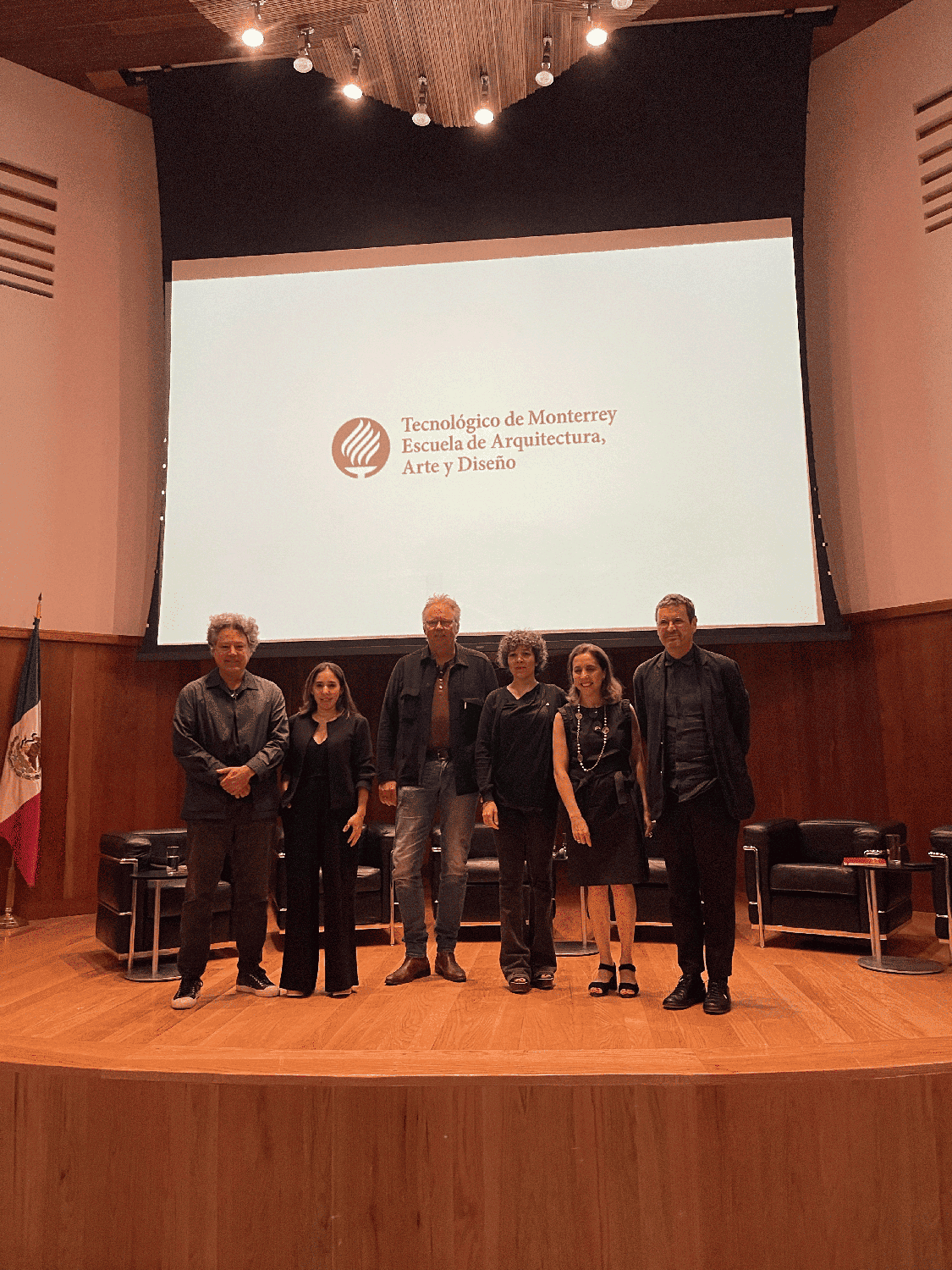Six people stand in front of a projector on a small stage.