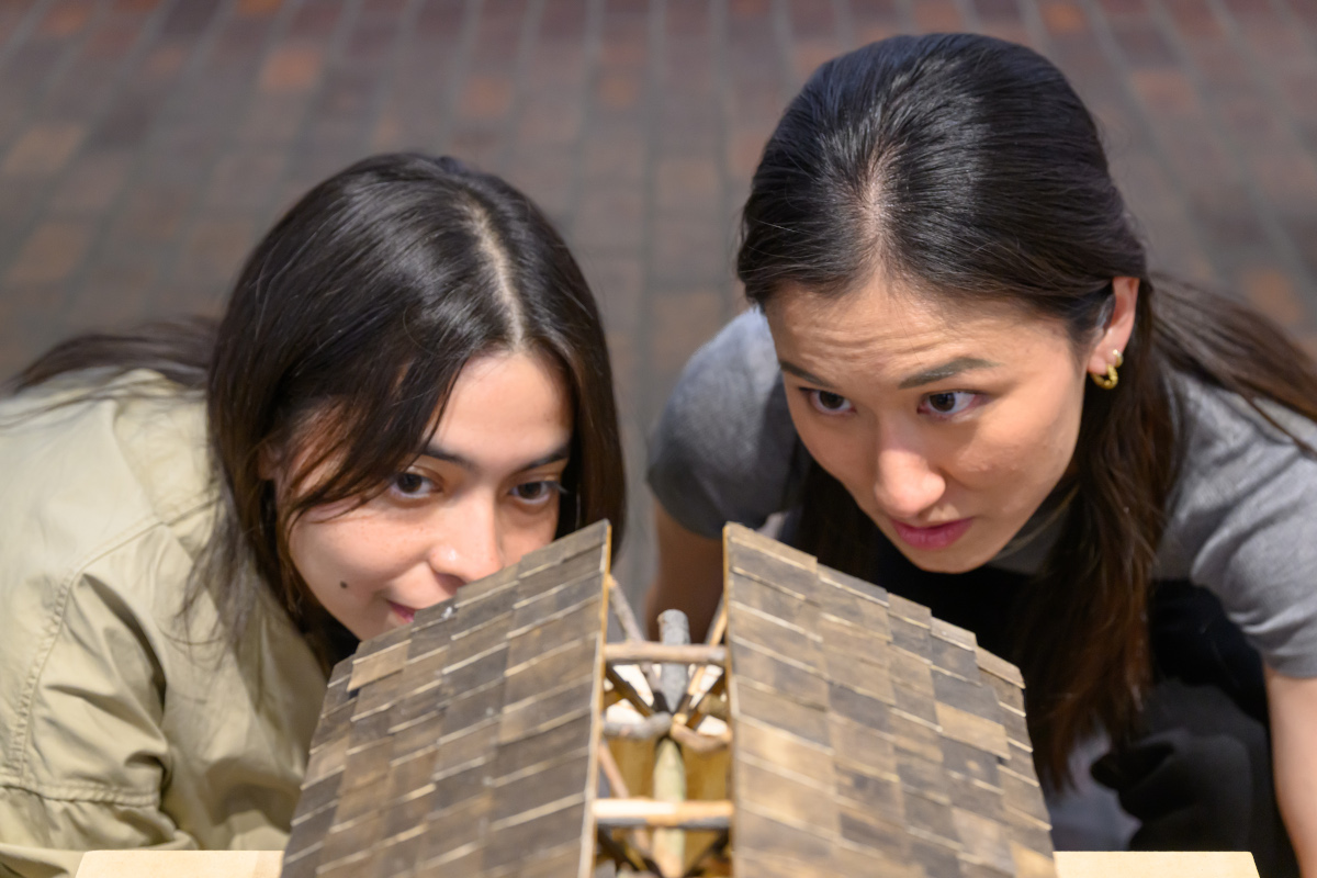 Two people look closely at an architectural model made of wood.