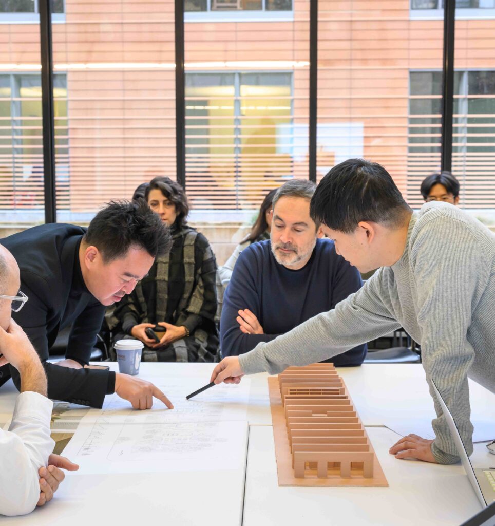 Students and instructors gather around architectural model and drawings on table