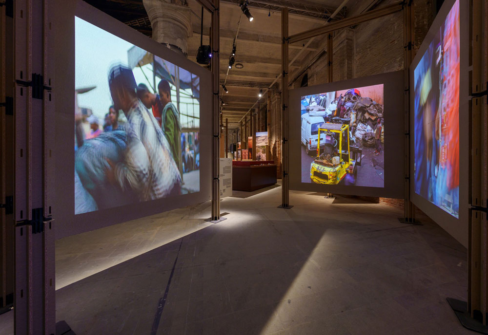 Three large screens with images of people and busy markets.