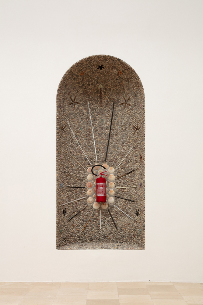 Fire extinguisher in stone encrusted niche.